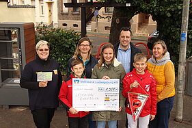 Bürgermeister Sacha Reichelt und Melanie Barth stehen gemeinsam mit Erwachsenen und Kindern aus Horrheim und einem Scheck über 1300 Euro auf dem Luisenplätzchen. 