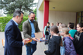 Bürgermeister Sacha Reichelt und Salih Yavuz verteilen Süssigkeiten an die Kinder der GGS Nordstadt.